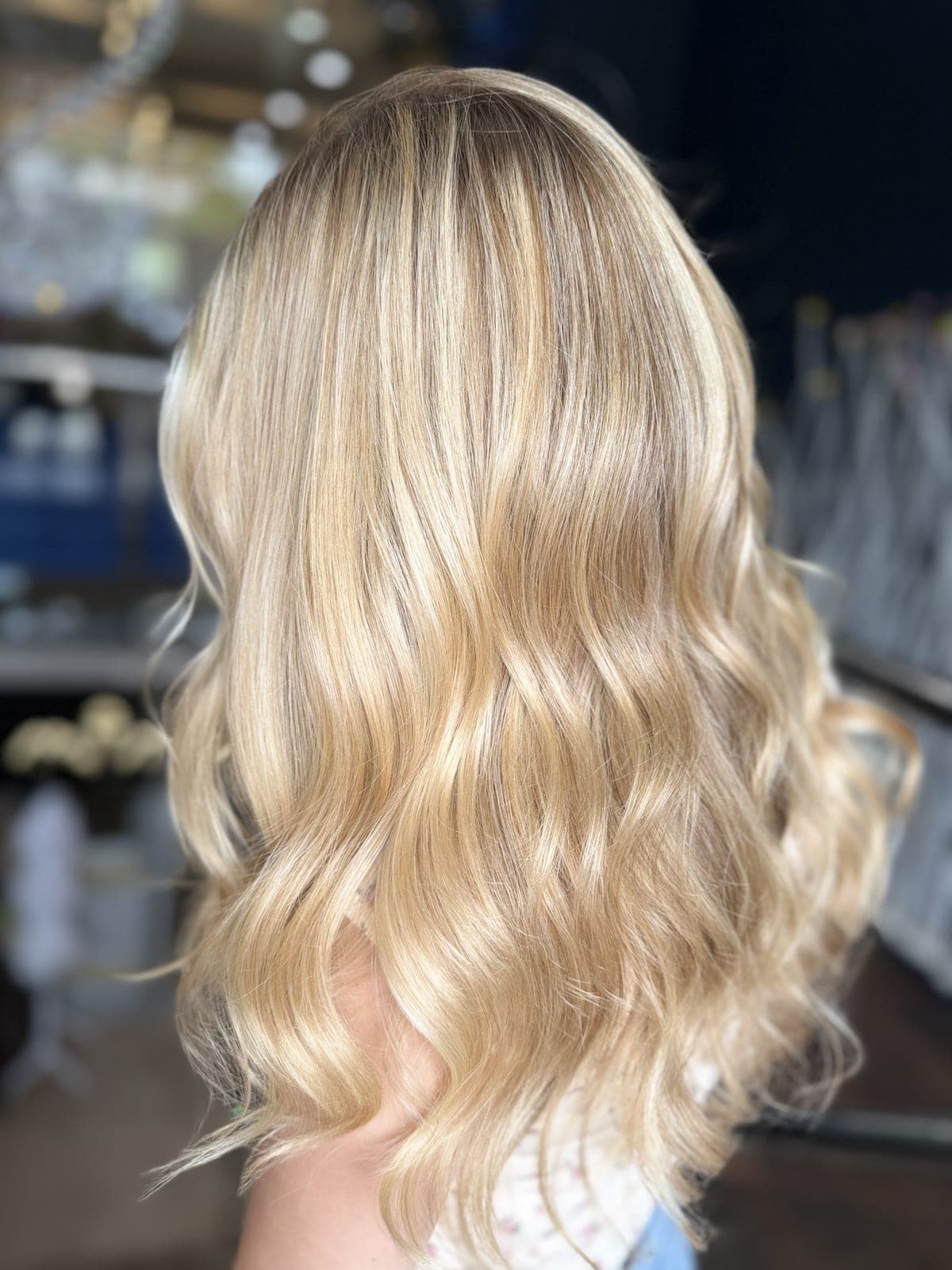 Buttery blonde balayage on long hair styled in glossy waves, seen from the side