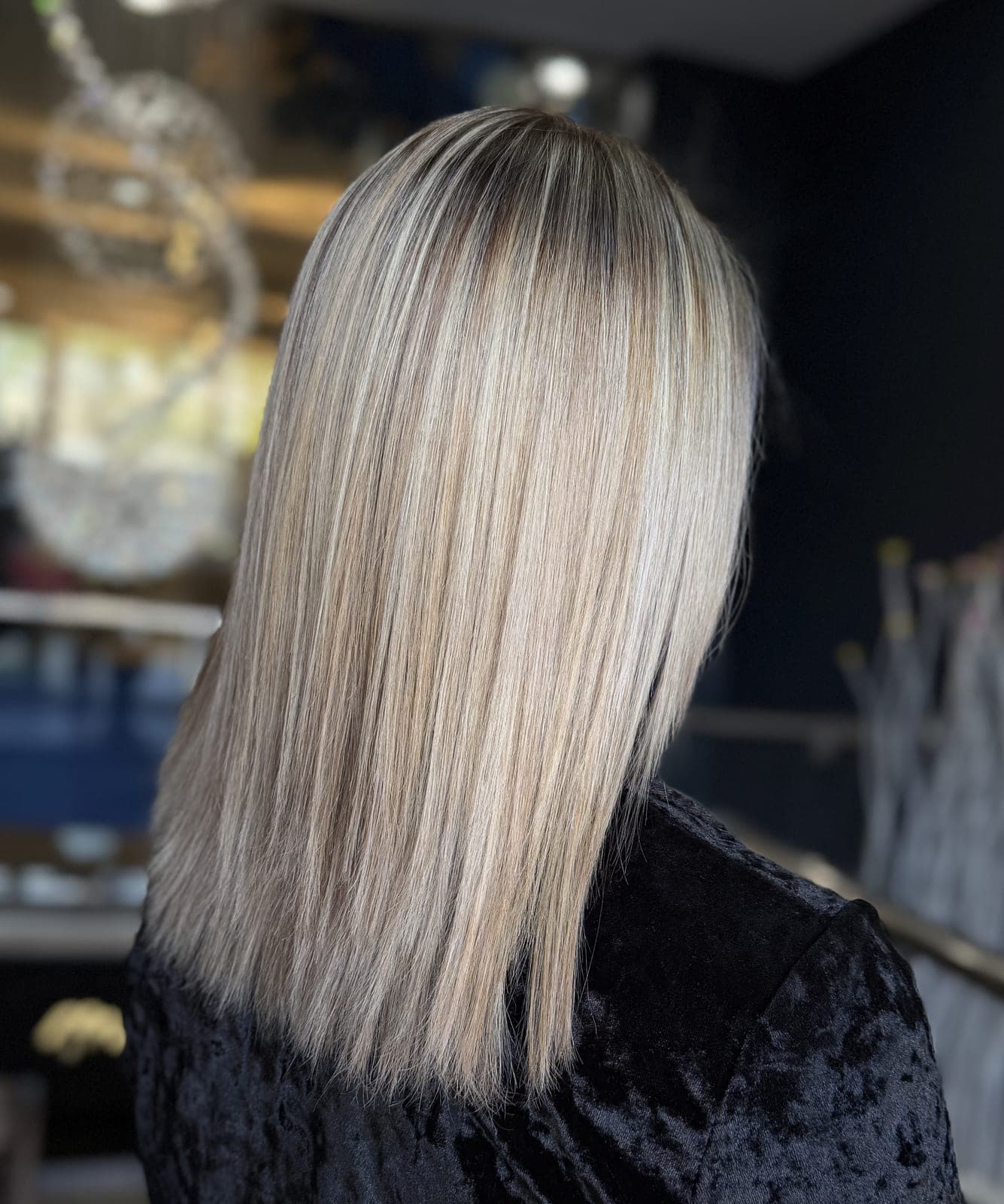 Cool blonde fine highlights on a straight shoulder-length cut, salon interior behind